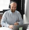 Smiling support representative wearing a headset, working on a laptop at a desk in a well-lit office