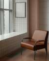 Moderner brauner Ledersessel in einem stilvollen Innenraum mit Fliesenwand, großem Fenster und minimalistischem Design.